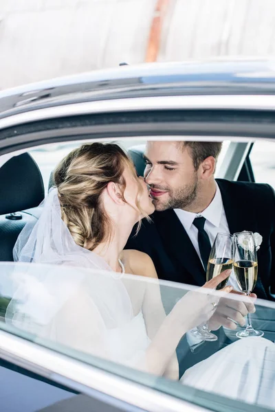 Atractiva novia y guapo novio besos y tintineo con copas de champán - foto de stock