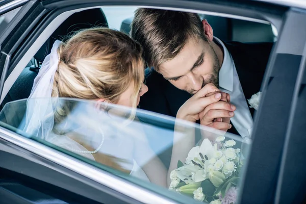 Красивый жених в костюме целует руку своей привлекательной невесты — стоковое фото