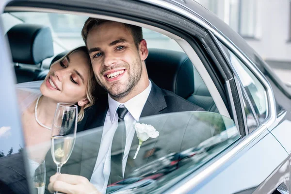 Attractive bride and handsome bridegroom smiling and holding champagne glass — Stock Photo