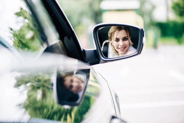 Reflexion der attraktiven und blonden Braut, die im Auto in den Spiegel schaut — Stockfoto