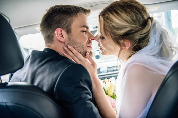 Vue arrière de la mariée attrayante dans le voile nuptial et baiser marié dans la voiture — Photo de stock