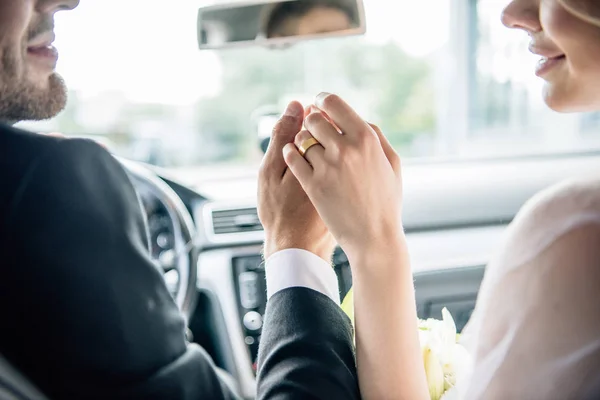 Cropped view of bridegroom and bride holding hands in car — Stock Photo