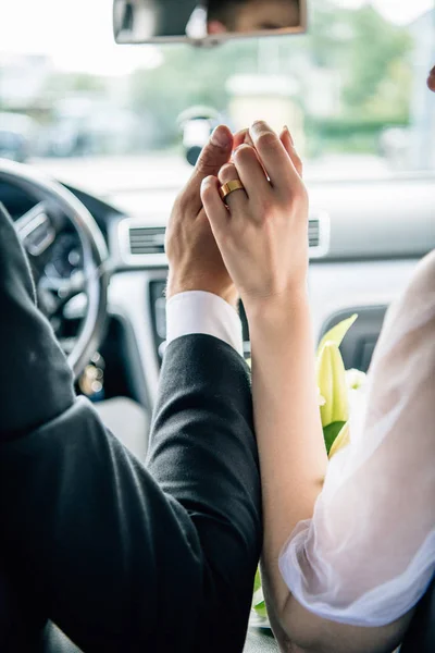 Vista cortada do noivo e noiva de mãos dadas no carro — Fotografia de Stock