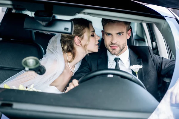 Belle mariée en voile nuptial embrasser beau marié en voiture — Photo de stock