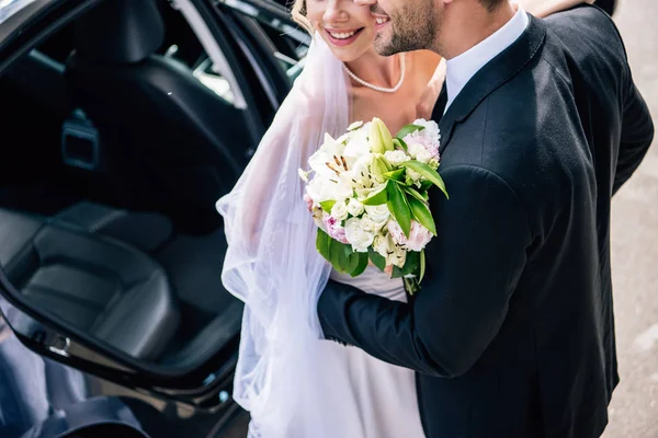 Abgeschnittene Ansicht des Bräutigams im Anzug umarmt Braut mit Strauß — Stockfoto