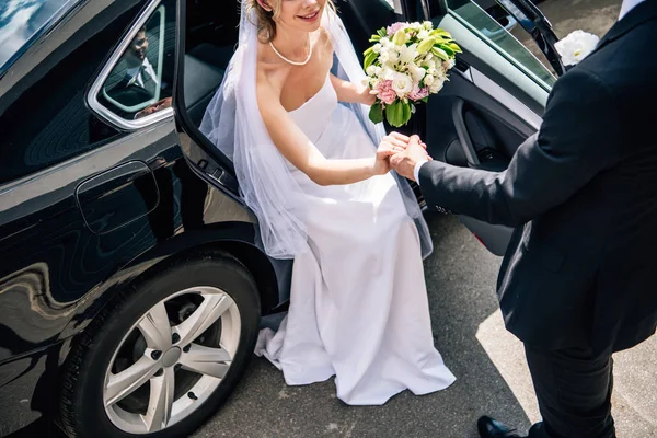 Vista cortada do noivo em terno dando a mão à noiva com buquê — Fotografia de Stock