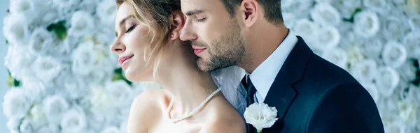 Panoramic shot of attractive bride and handsome bridegroom hugging with closed eyes — Stock Photo