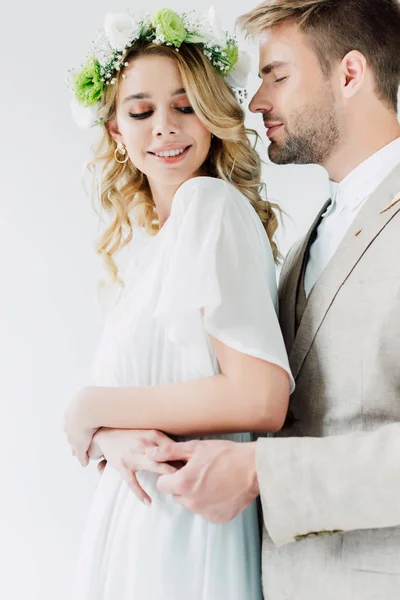 Beau marié en costume câlin avec mariée en robe de mariée et couronne isolé sur blanc — Photo de stock