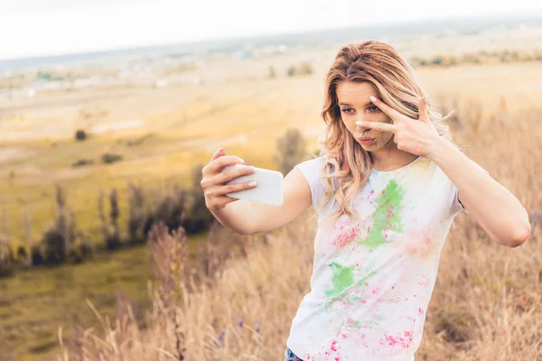 Atractiva mujer en camiseta tomando selfie y mostrando señal de paz - foto de stock
