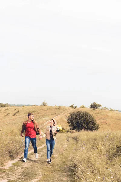 Mujer atractiva con ramo y hombre guapo sonriendo y tomados de la mano - foto de stock