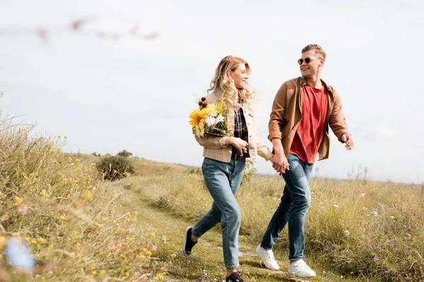 Attractive woman with bouquet and handsome man smiling and holding hands — Stock Photo
