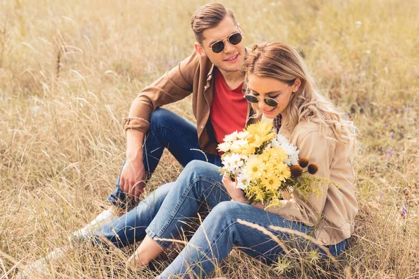 Attraktive Frau mit Blumenstrauß und schöner Mann, der lächelt und draußen sitzt — Stockfoto