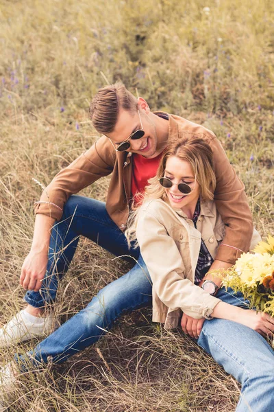 Mujer atractiva con ramo y hombre guapo sonriendo y sentado fuera - foto de stock