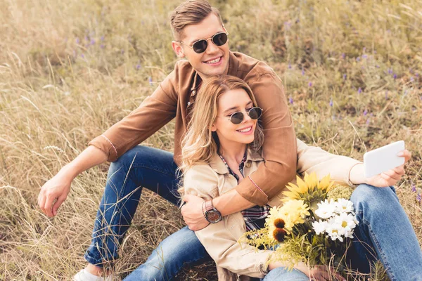 Attraktive Frau mit Blumenstrauß und schöner Mann, der lächelt und draußen sitzt — Stockfoto