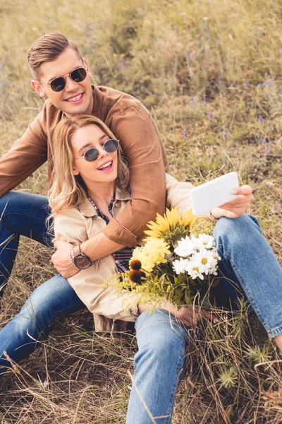 Femme attrayante avec bouquet et bel homme prenant selfie — Photo de stock