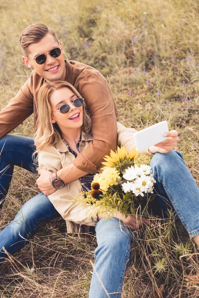 Attraktive Frau mit Blumenstrauß und schöner Mann, der ein Selfie macht — Stockfoto