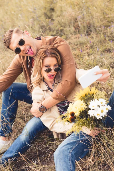 Attraktive Frau mit Blumenstrauß und schöner Mann, der ein Selfie macht — Stockfoto