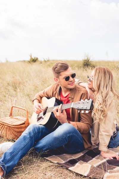 Guapo hombre tocando la guitarra acústica y atractiva mujer abrazándolo - foto de stock