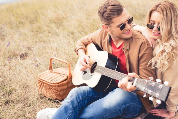 Guapo hombre tocando la guitarra acústica y atractiva mujer abrazándolo - foto de stock