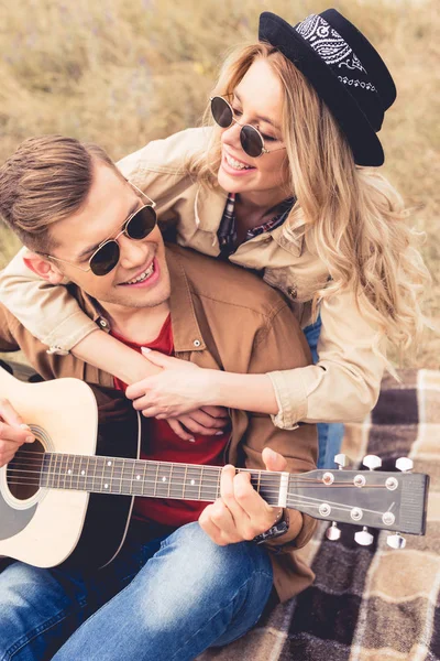 Guapo hombre tocando la guitarra acústica y atractiva mujer abrazándolo - foto de stock