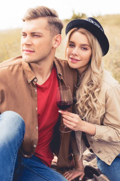 Bel homme regardant loin et femme attrayante dans le chapeau tenant verre de vin — Photo de stock