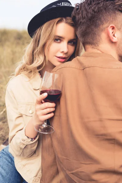 Atractiva mujer en sombrero sosteniendo copa de vino y abrazando al hombre - foto de stock