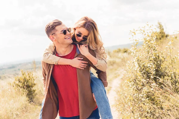 Schöner Mann huckepack seine attraktive und blonde Freundin draußen — Stockfoto