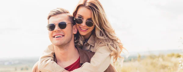 Plano panorámico de hombre guapo a cuestas su atractiva y rubia novia fuera - foto de stock