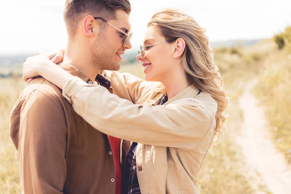 Vista laterale di donna attraente abbracciando bello uomo in occhiali da sole — Foto stock