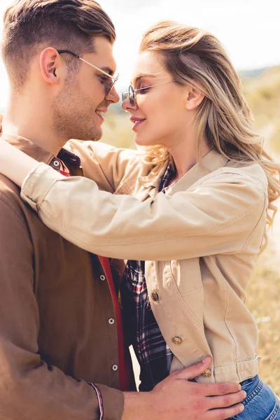 Vista lateral da mulher atraente abraçando e beijando com homem bonito em óculos de sol — Fotografia de Stock