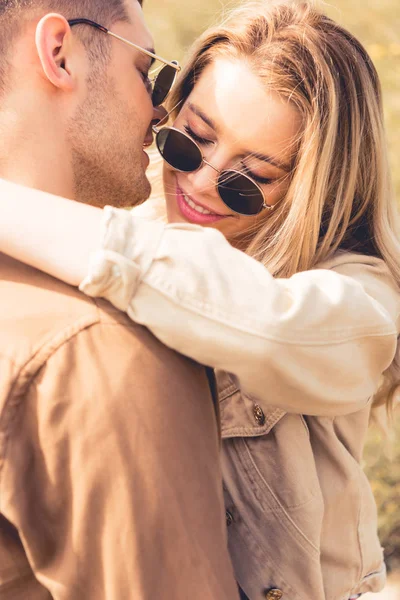 Mulher atraente abraçando e beijando com homem bonito em óculos de sol — Fotografia de Stock