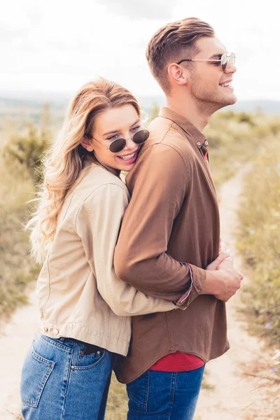 Attraktive und lächelnde Frau umarmt gutaussehenden Mann mit Sonnenbrille — Stockfoto