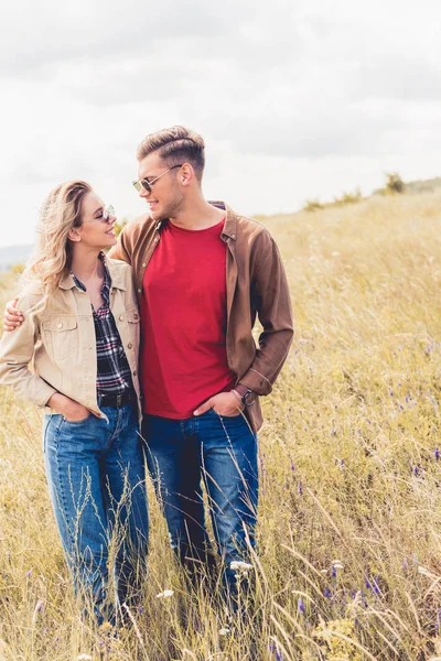 Mujer atractiva y hombre guapo en gafas de sol abrazándose fuera - foto de stock