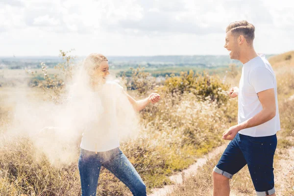 Attraktive Frau und gutaussehender Mann in T-Shirts, die buntes Puder werfen — Stockfoto