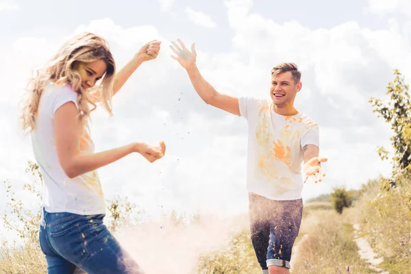 Mujer atractiva y hombre guapo en camisetas lanzando polvo colorido - foto de stock