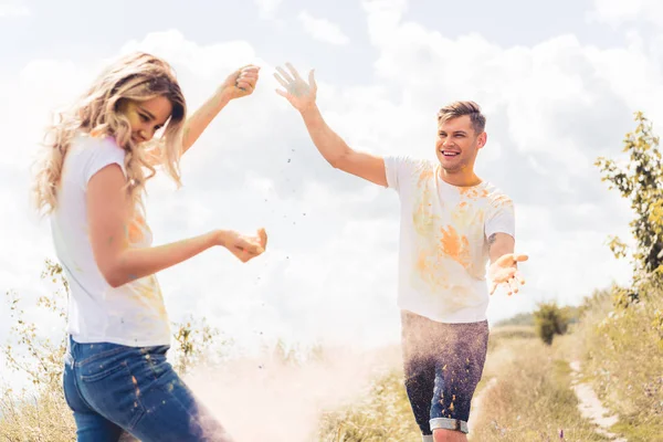 Attraktive Frau und gutaussehender Mann in T-Shirts, die buntes Puder werfen — Stockfoto