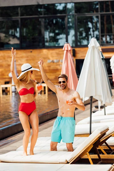 Повний вигляд щасливої усміхненої пари, що тримає коктейлі на курорті в сонячний день — стокове фото