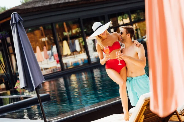 Full length view of happy smiling couple holding cocktails and embracing at resort in sunny day — Stock Photo