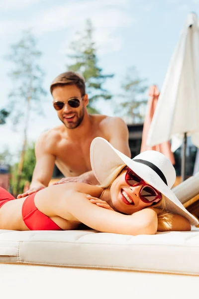 Sonriente hombre en gafas de sol haciendo masaje para novia en resort - foto de stock