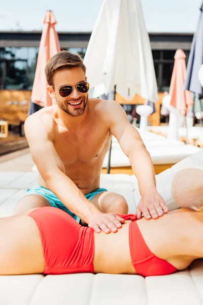 Sorrindo homem em óculos de sol fazendo massagem para namorada no resort — Fotografia de Stock