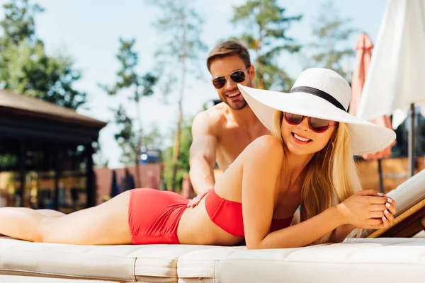 Smiling man in sunglasses doing massage for girlfriend at resort — Stock Photo
