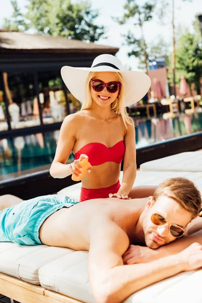 Sonriente sexy chica aplicando protector solar en novio en resort - foto de stock