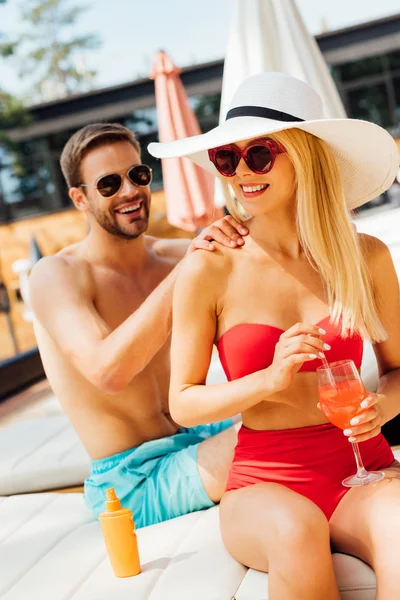 Smiling man in sunglasses doing massage for girlfriend at resort — Stock Photo