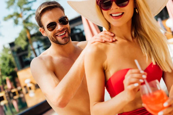 Sorrindo homem em óculos de sol fazendo massagem para namorada no resort — Fotografia de Stock