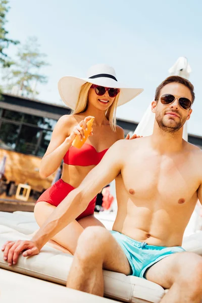 Усміхнена сексуальна дівчина наносить сонцезахисний крем на хлопця на курорті — стокове фото