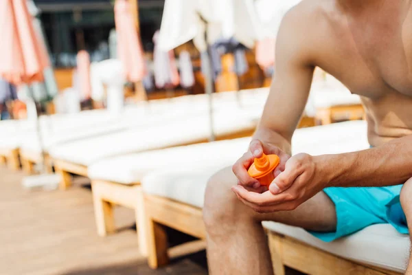Частковий вид без сорочки чоловік сидить на шезлонгу і наносить сонцезахисний крем на курорт — стокове фото