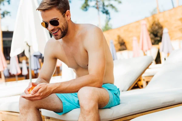 Hemdloser Mann sitzt auf Liege und trägt Sonnencreme am Urlaubsort auf — Stockfoto