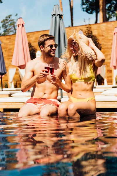 Sexy couple holding glasses of red wine and smiling in swimming pool — Stock Photo