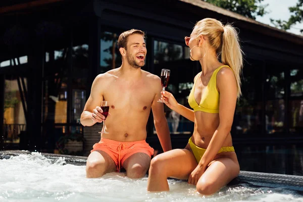 Sexy pareja sosteniendo vasos de vino tinto en la piscina - foto de stock