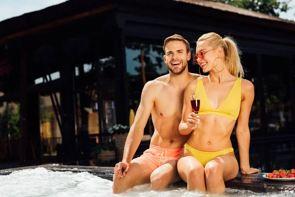 Sexy pareja sonriente con vino tinto y fresas en la piscina - foto de stock